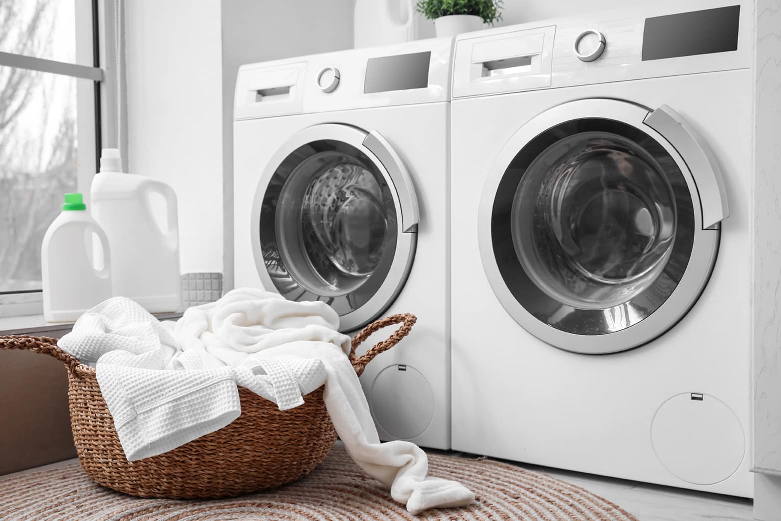 - Sam's Appliance Repair Modern white washing machine and dryer with a wicker laundry basket filled with white towels, next to detergent bottles in a bright laundry room.