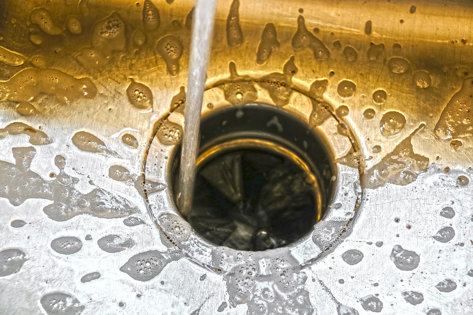 Water running into a garbage disposal of a stainless steel sink.